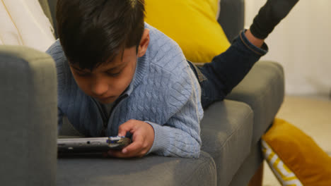 Young-Boy-Lying-On-Sofa-At-Home-Playing-Game-Or-Streaming-Onto-Handheld-Gaming-Device-4